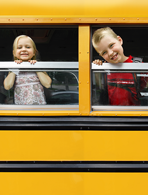 Two smiling students peeking their heads out of bus windows